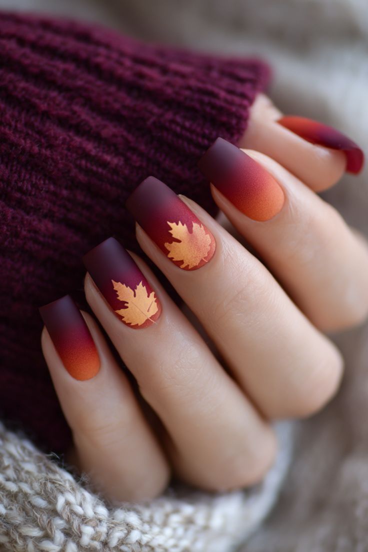 Burgundy to orange ombre short square nails with a gold maple leaf accent, burgundy knit sleeve