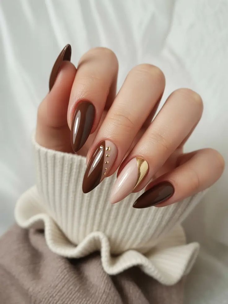 Chocolate almond nails with a gold swirl accent nail, hand in a cream ruffle sweater