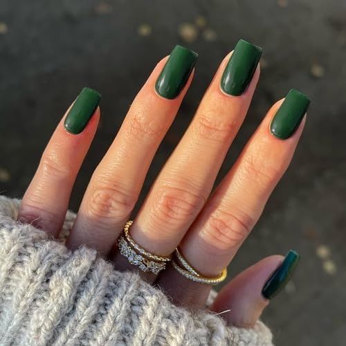 Forest green coffin nails on a hand in a grey knit sweater with gold rings, glossy dark green gel