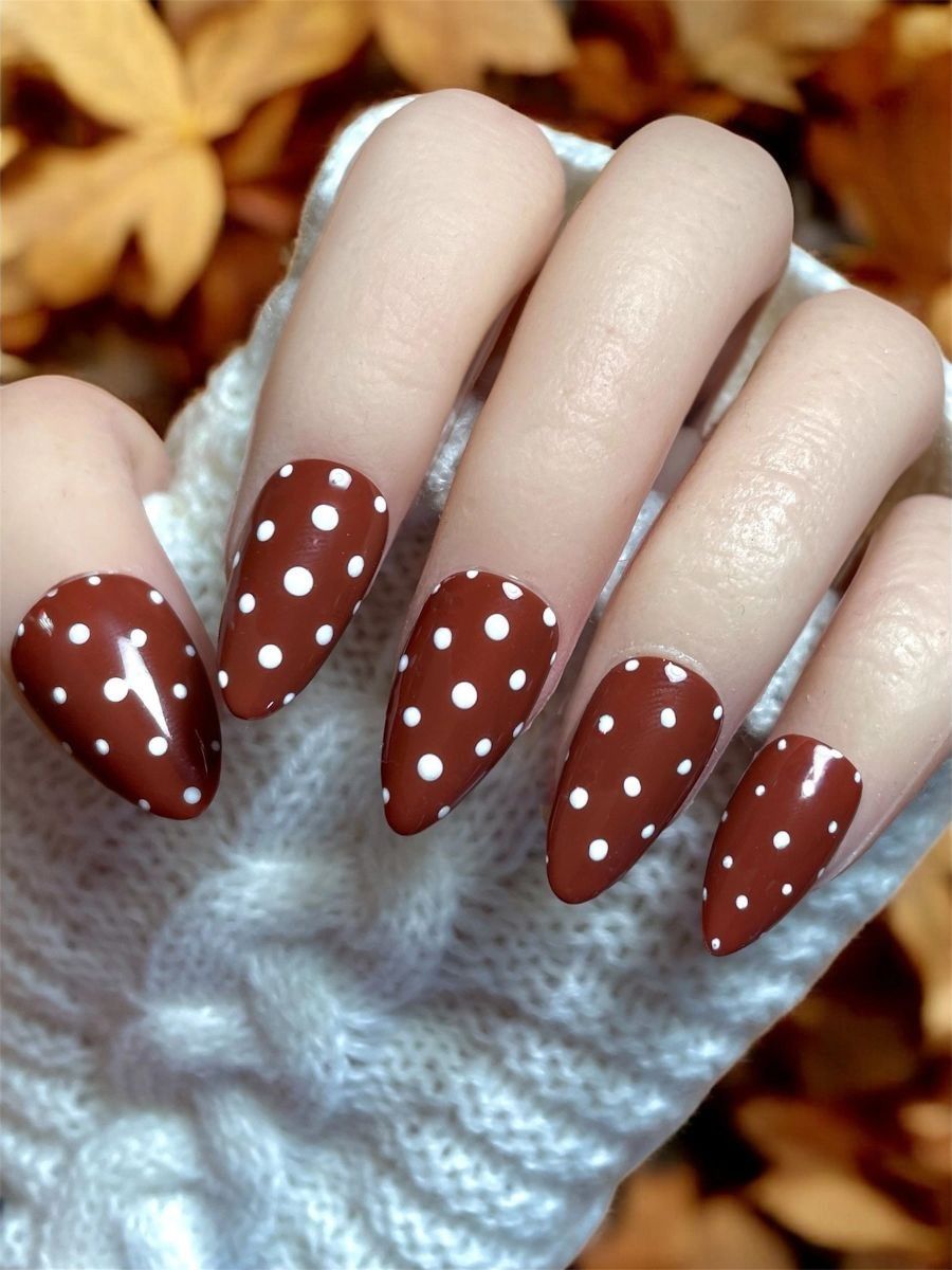 Rust polka dot almond nails with cream dots on a burnt rust gel, hand in a white knit glove