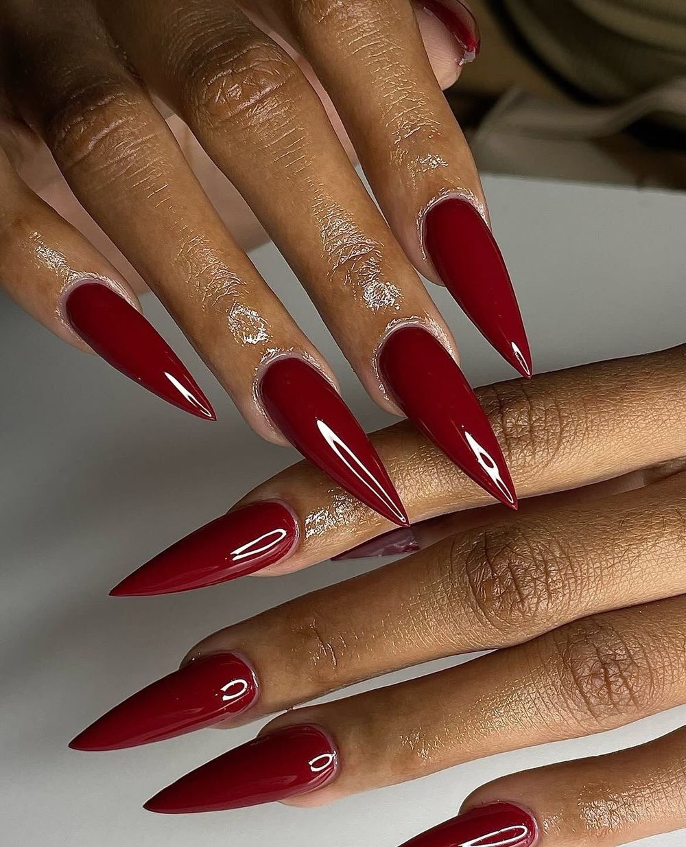 Cherry red stiletto nails, long sharp points in a bright glossy red on brown skin