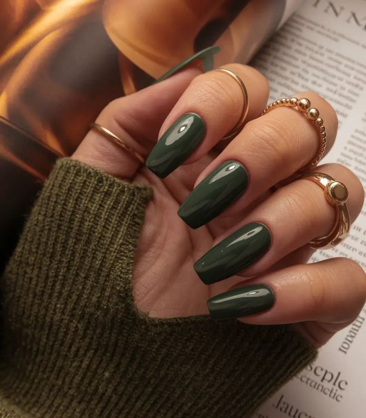 Deep forest green nails on brown skin, glossy dark green gel worn with a green knit and gold rings