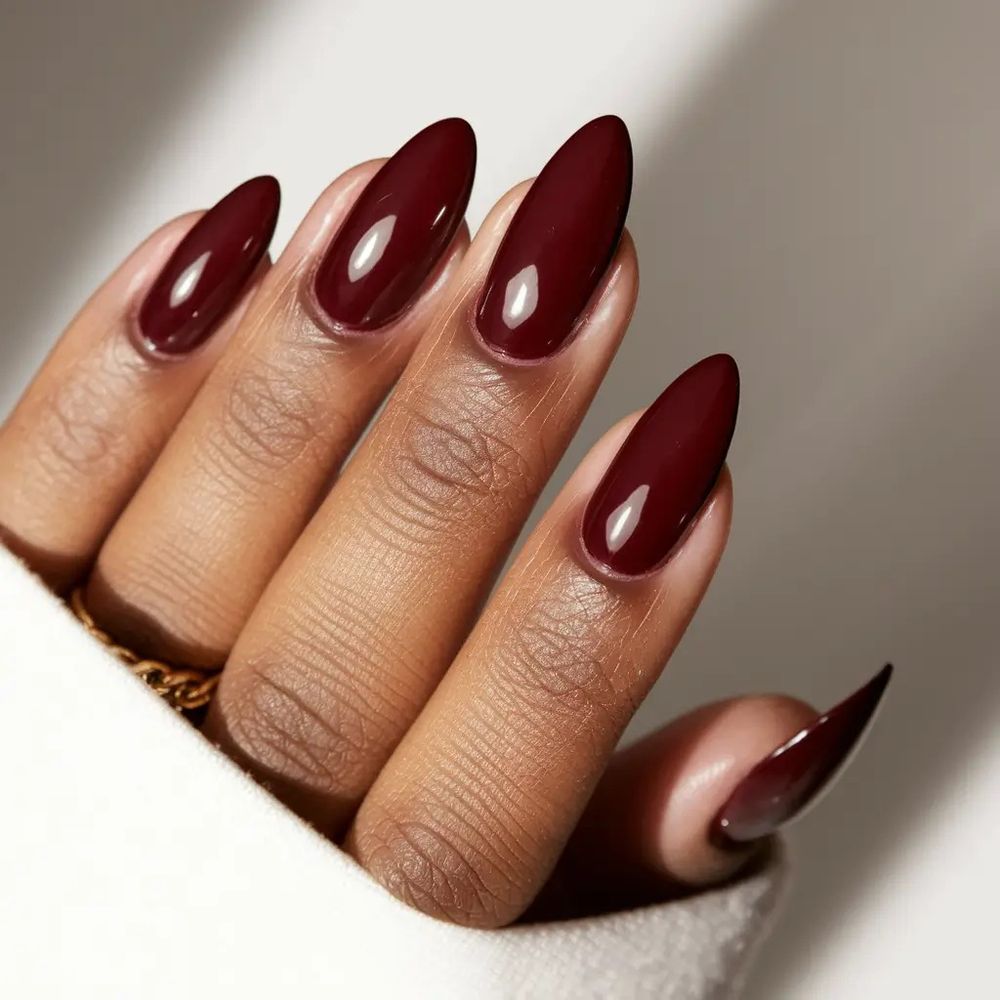 Glossy burgundy almond nails on dark skin, long oval almond shape with a high shine gel finish