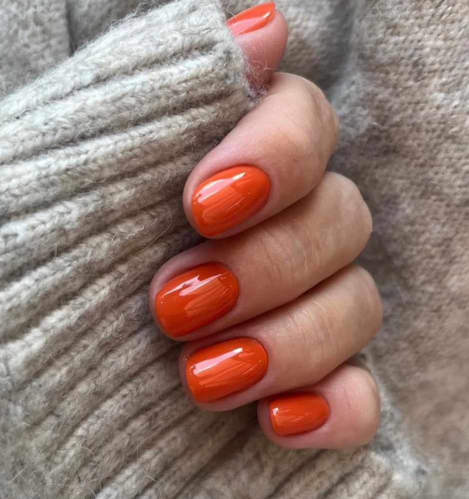 Pumpkin spice short round nails, glossy orange gel on a short natural length in a grey sweater