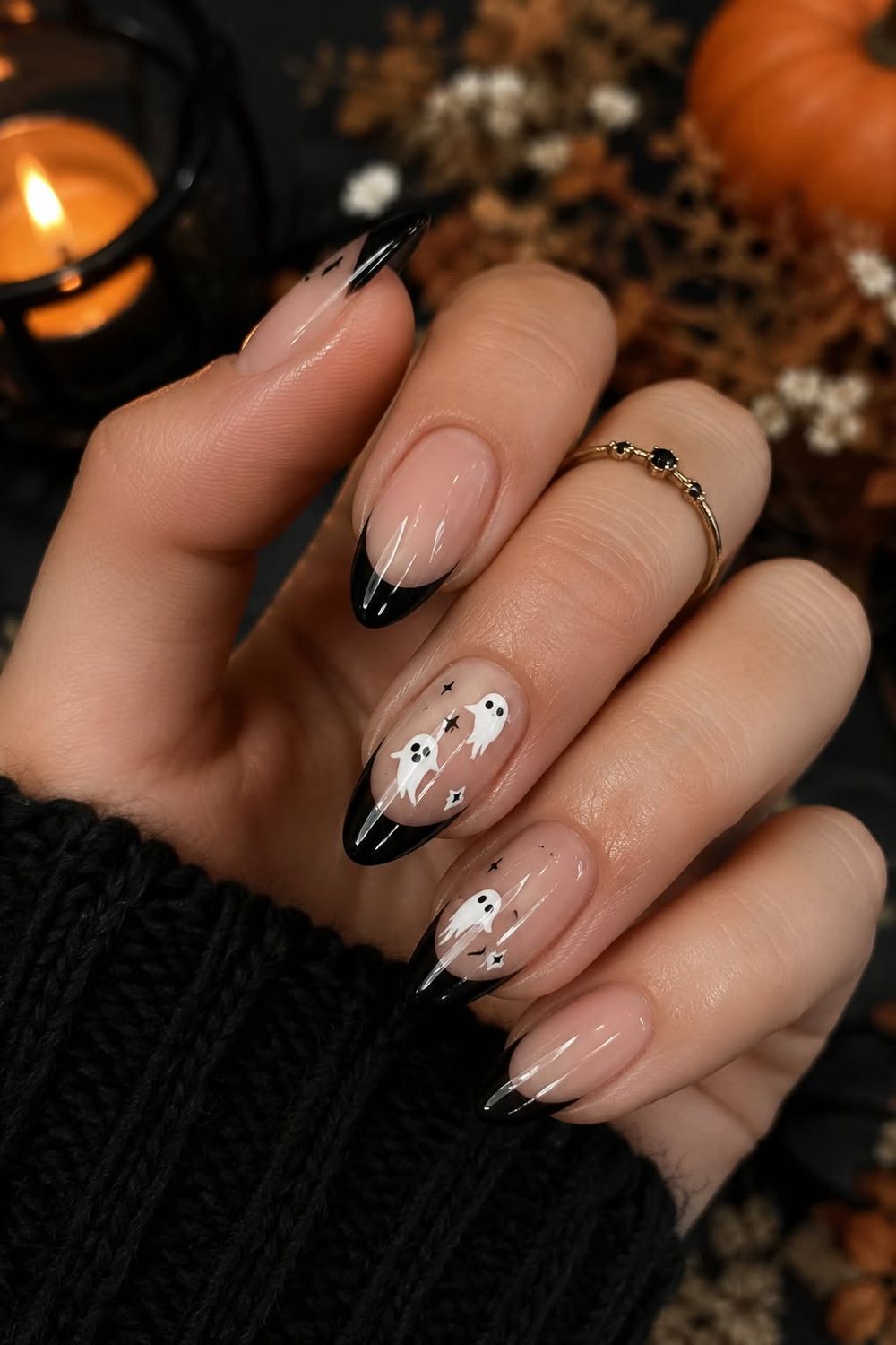 Subtle Halloween nails with black French tips and a tiny ghost accent nail on a nude base, pumpkins in the background
